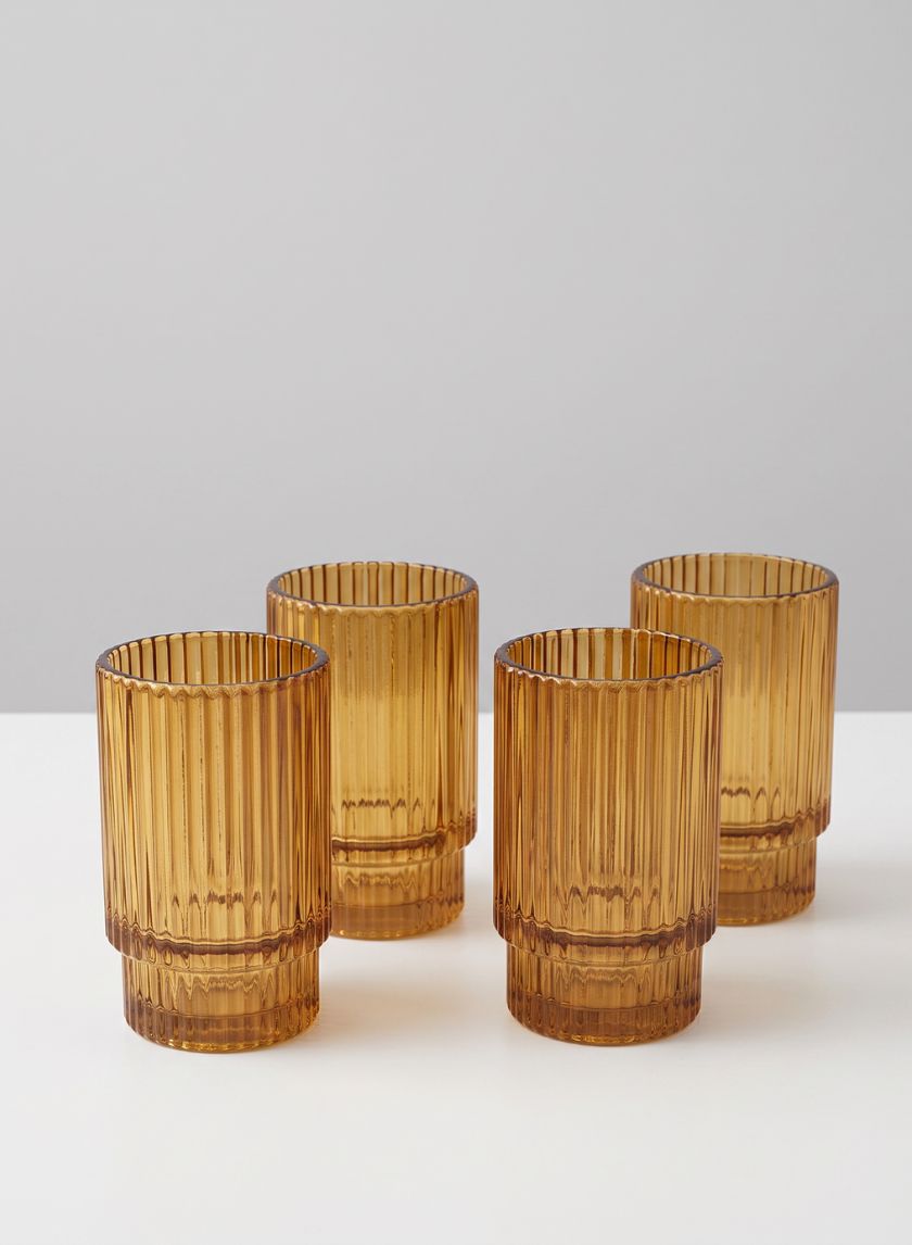 A set of four 3.75-inch tall amber pleated glass votive holders is arranged on a white surface against a light gray background.
