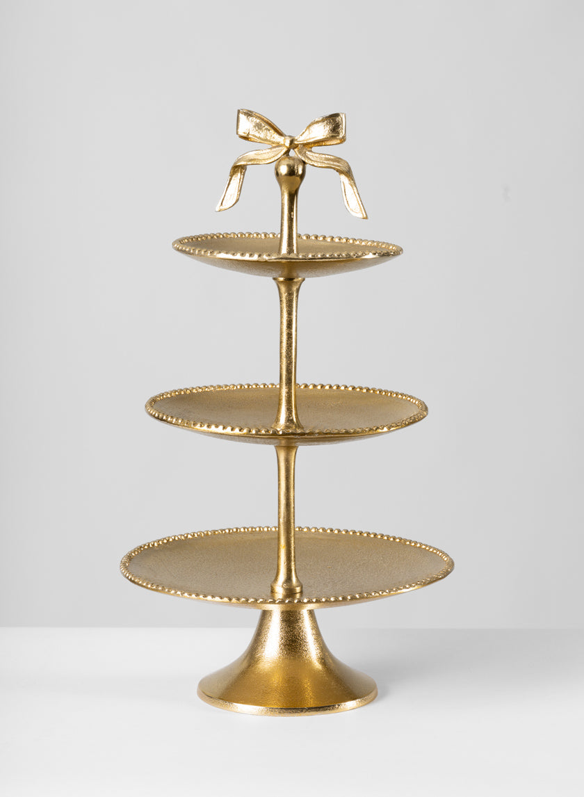 The 21in Tall Atelier 3 Tier Gold Display Stand features beaded edges and a decorative bow on top, displayed on a white surface with a plain light gray background.