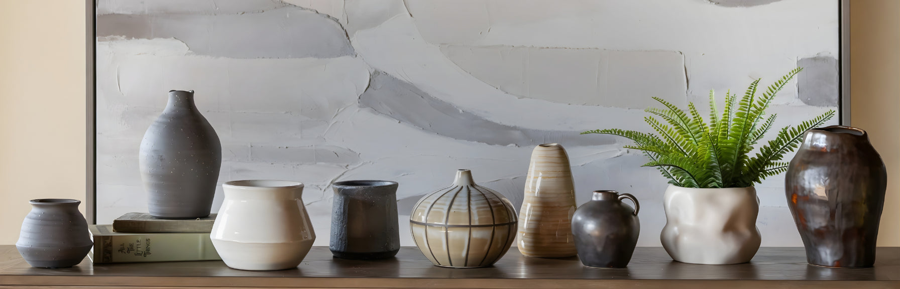 Collection of various ceramic vases on a shelf with a abstract painting in the background