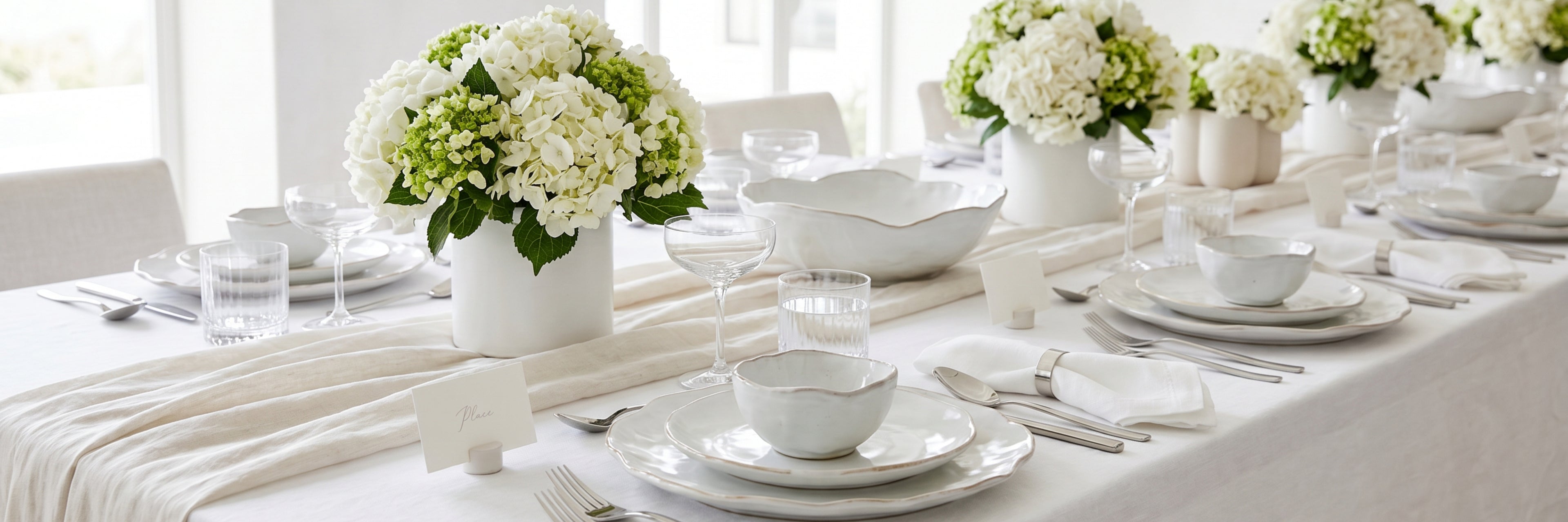 Elegant dining table setting with white tablecloth, plates, bowls, and floral arrangements.