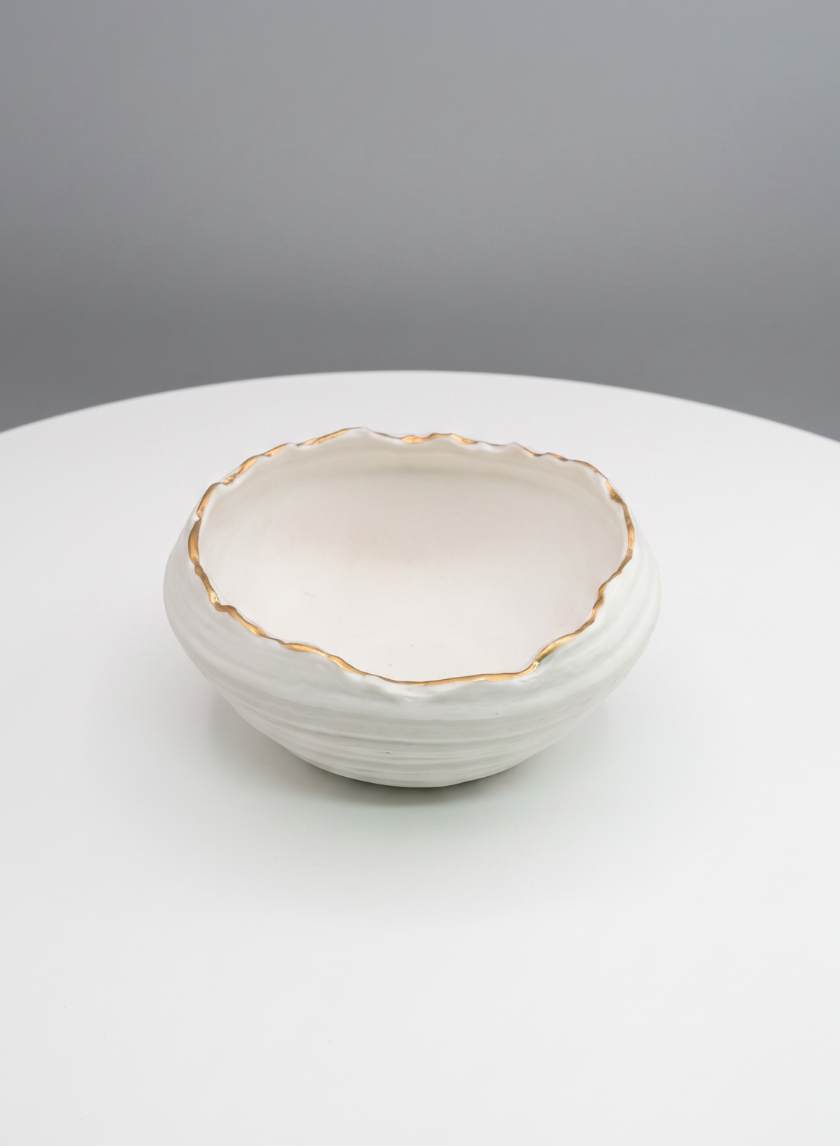 A 6in Clay White Porcelain Bowl with Gold Edging sits on a round white table against a gray background.