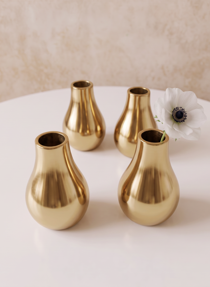 Four 4in Tall Shiny Gold Bud Metal Vases are arranged on a round white table, with a single white flower displayed in one vase. The background features a softly textured beige tone.