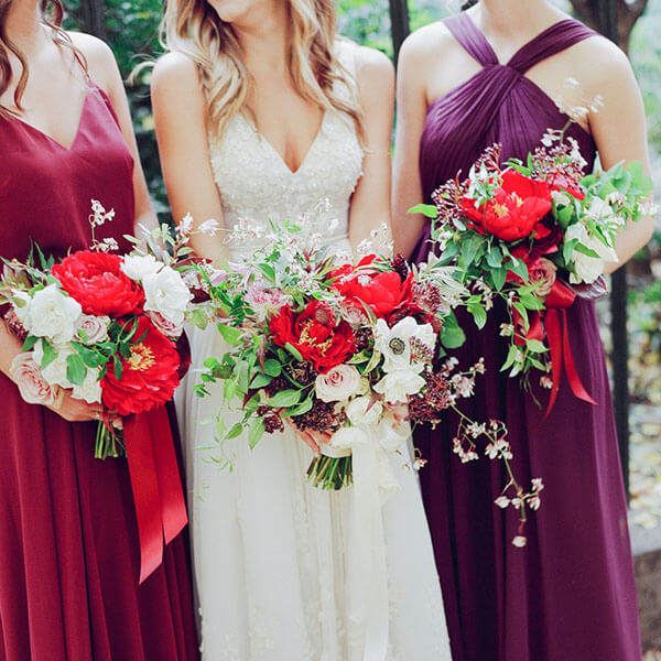 bride and two bridesmaids with their bouquets of red tree peonies blush roses and plum-colored berries
