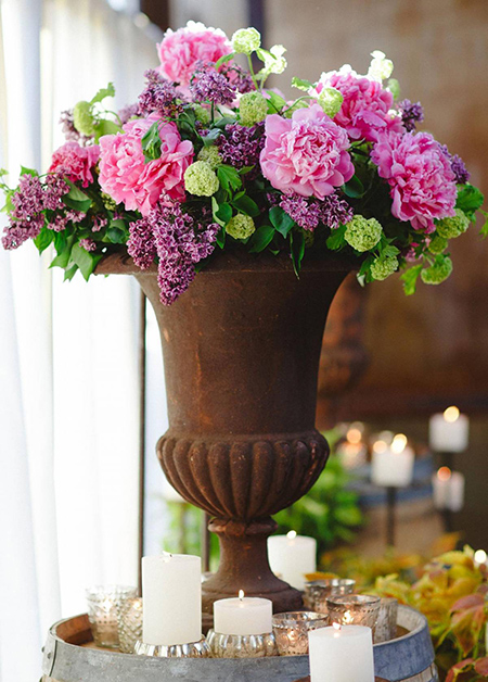 A rust brown urn filled with peonies, lilac, and viburnum, is surrounded by our mercury glass bowls and votives at this Brooklyn wedding Rebecca designed.
