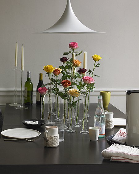 pedestal bud vases on a dinner table each with a single rose in different colors