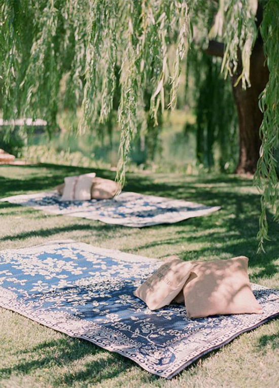 carpets layed out under trees with pillows for wedding guests to relax
