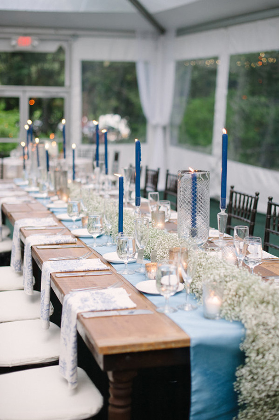 long wedding reception table in a tent with blue runner and blue dinner candles in glass candlesticks and baby's breath floral table runner