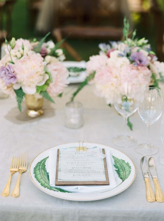 place setting with plate with leaf motif holding menu with gold gold clip gold flatware and peony centerpieces in gold vases