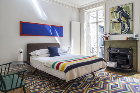 bedroom with white linens and colorful striped blanket and rug