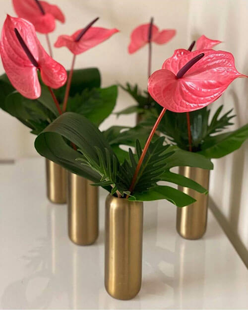 pink anthuriums with philodendron leaves in gold bud vases