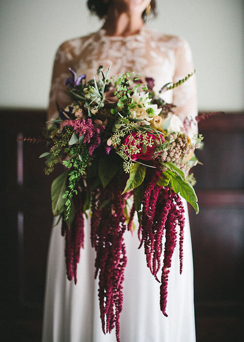 the knot bride holding cascading wedding bouquet with amaranth protea roses maidenhair ferns