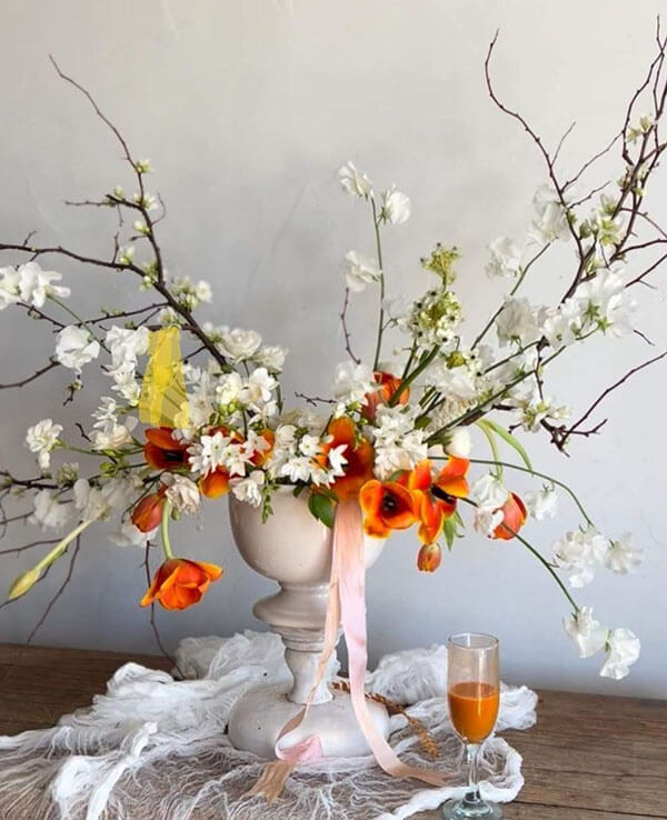 freeform floral arrangement using cherry blossoms and orange tulips in white ceramic bowl