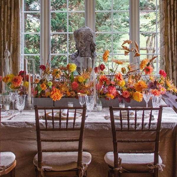 fall dining table with long centerpiece in gray window boxes with foliage orange and yellow dahlias and chrysanthemums