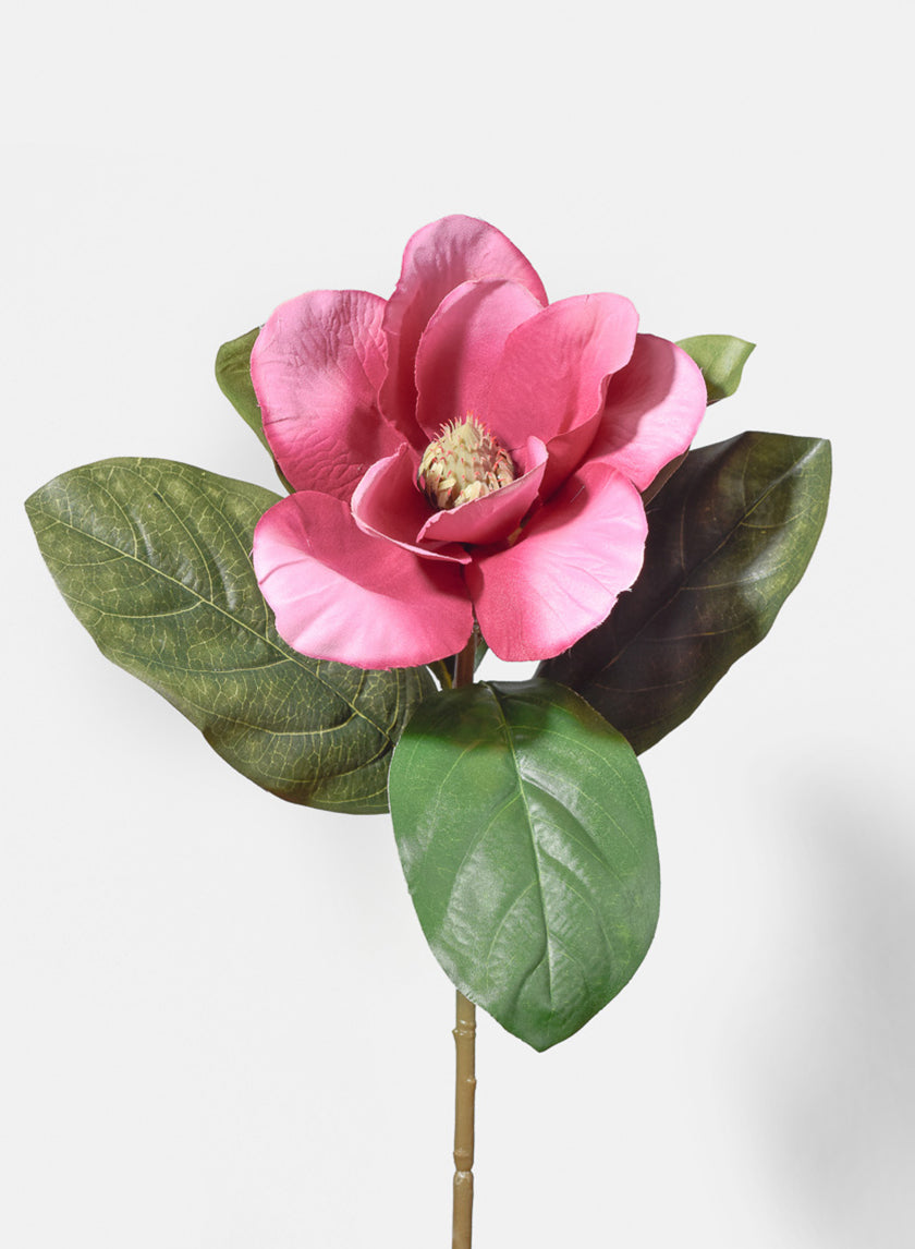 A single pink artificial flower with multiple petals and a yellow center, surrounded by large green leaves, against a plain white background.