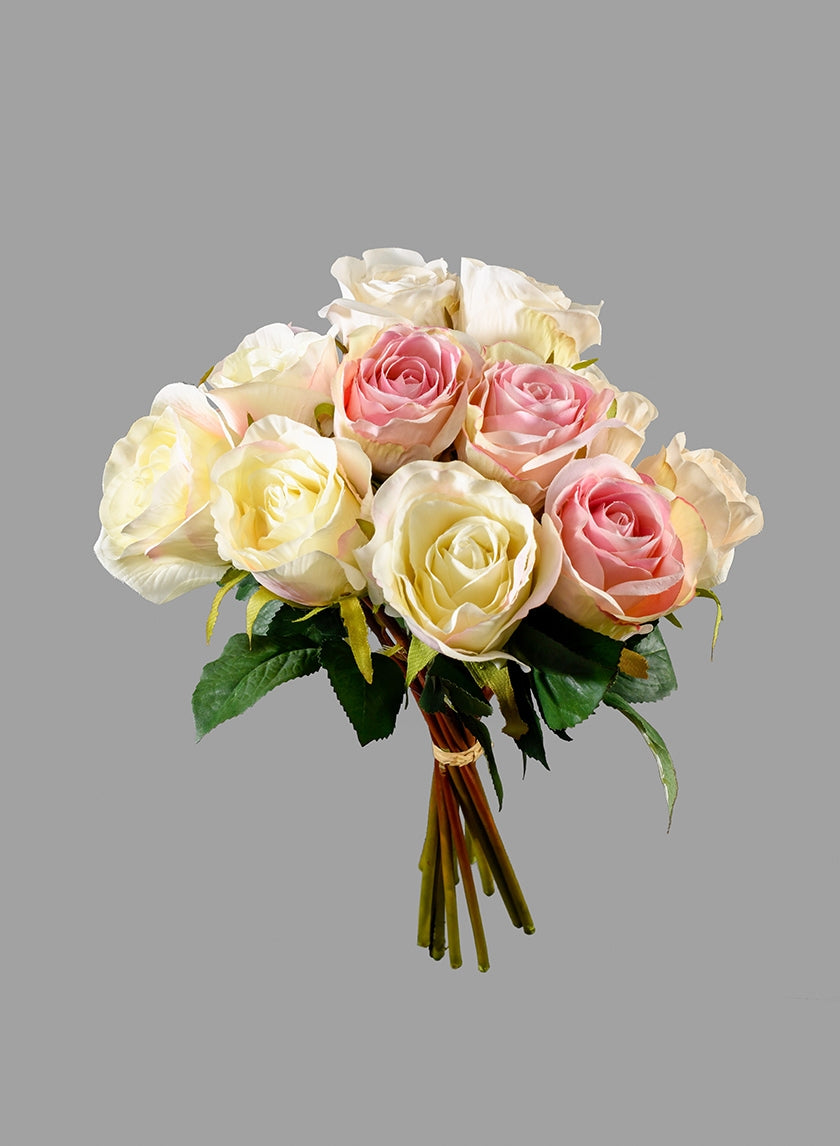 A bouquet of artificial roses featuring pale yellow and pink flowers with green leaves, tied together with a brown string, set against a plain gray background.