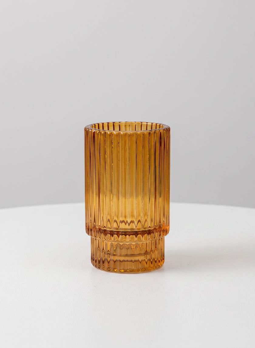 A 3.75in tall amber pleated glass votive holder from a set of 4 is displayed on a white surface against a plain light gray background.