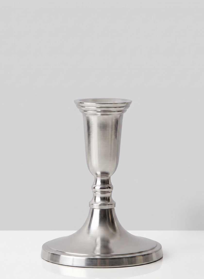 A 5.5in Tall Nickel Silver Candlestick with a wide base and a simple, polished design is placed on a white surface against a plain light gray background.