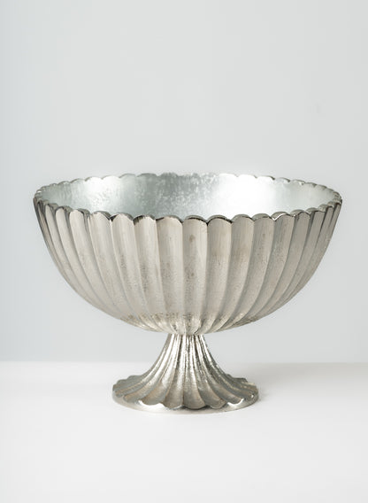 The 12in Palermo Brushed Silver Scallop Compote Metal Bowl features a metallic, fluted pedestal form with a reflective, scalloped edge, showcasing an elegant vintage-inspired design against a plain light gray background.