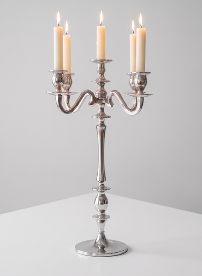 A 25.75in Tall Silver Metal Candelabra with five lit cream-colored candles stands on a white surface against a plain light gray background.