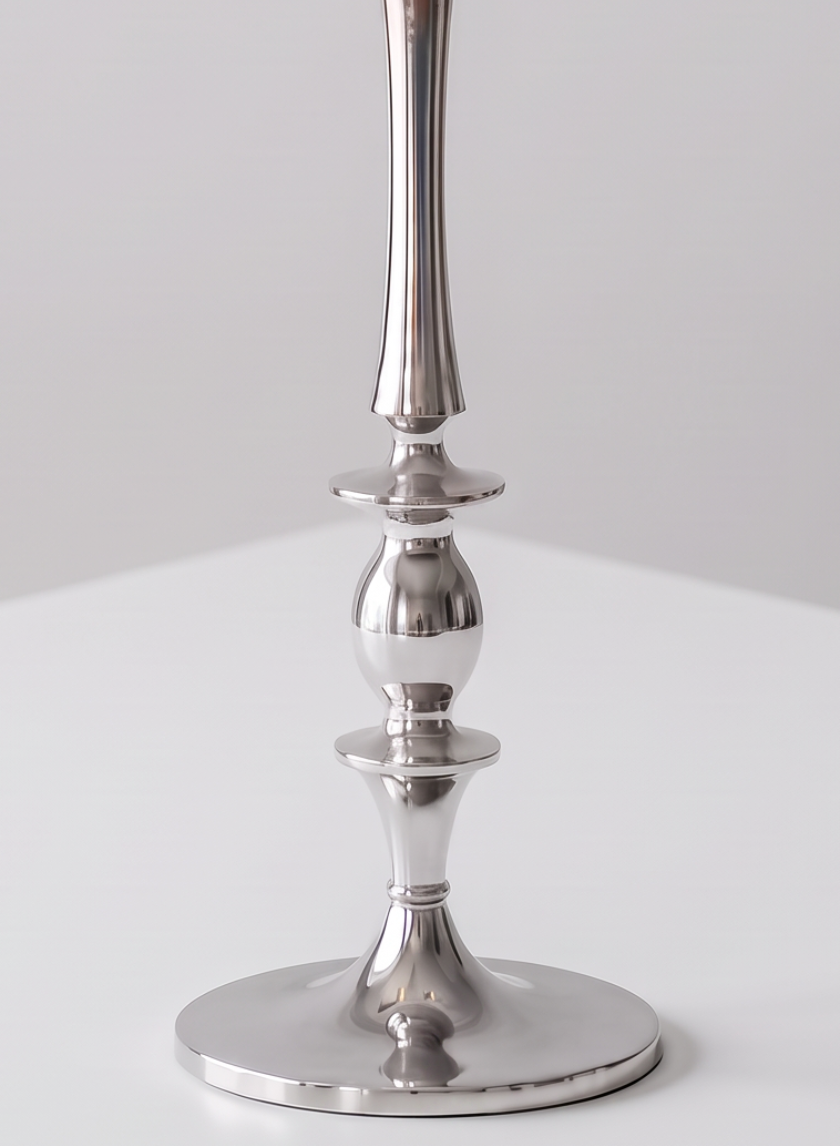 A close-up of the 25.75in Tall Silver Metal Candelabra on a white surface highlights its smooth, reflective finish and intricately shaped stem.
