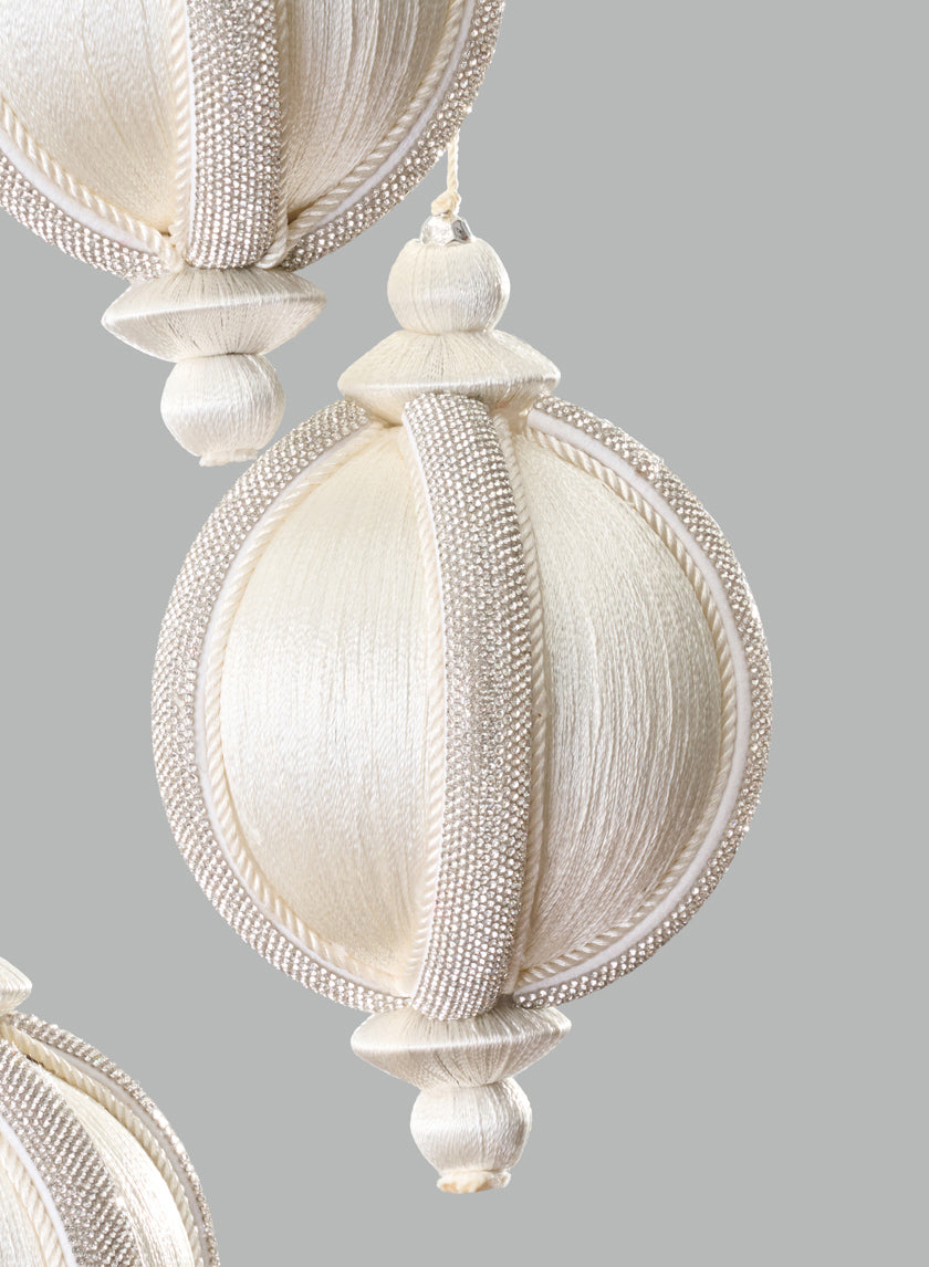 Three ornate 4in Round Rhinestone Wrapped White Hanging Decorative Ornaments, featuring textured surfaces and beadwork, hang against a plain gray background.