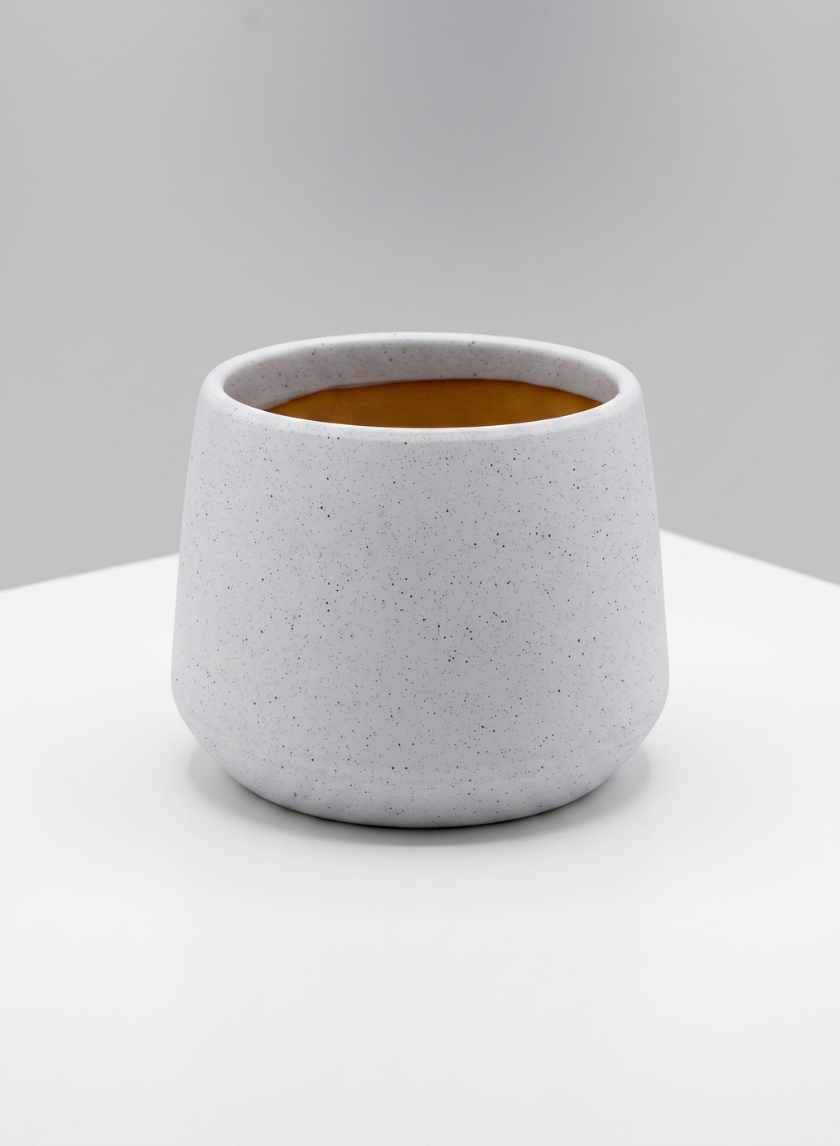 A 4in Tall Florist Choice Matte White Bell Cachepot, shown here with a round silhouette and speckled ceramic finish, features a wide opening and sits on a white surface against a light gray background. The interior of the cachepot displays a warm brown hue.