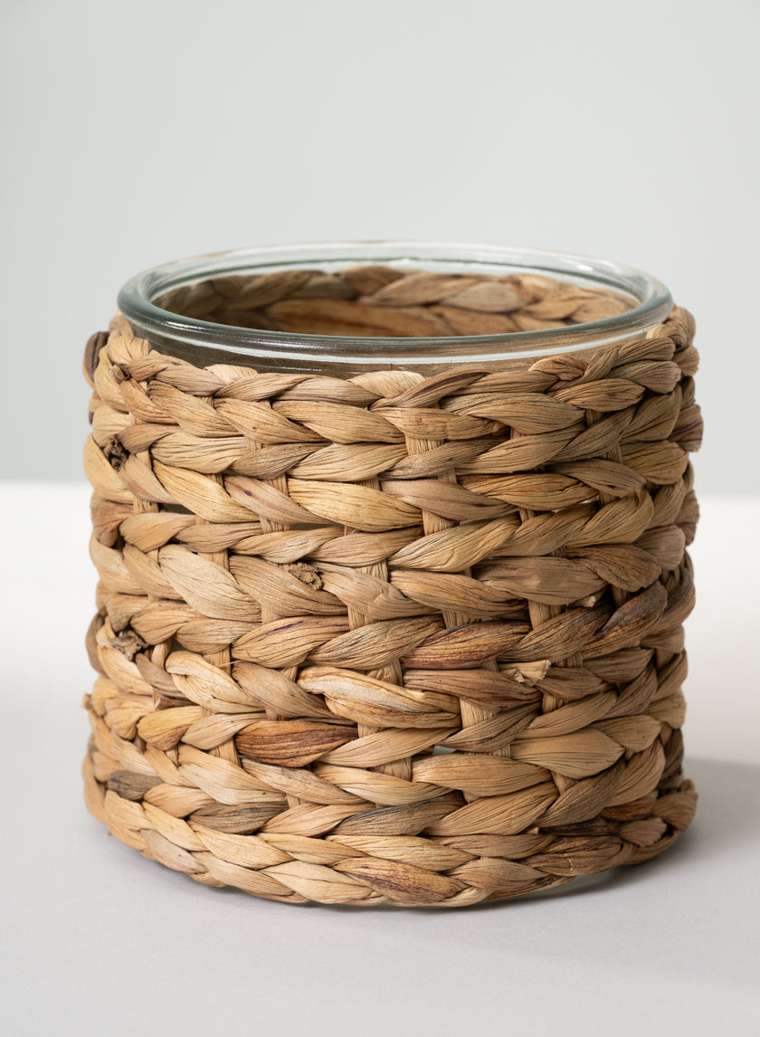 A 5in Tall Da Nang Hyacinth Glass Vase, featuring a round glass body wrapped in natural-colored woven hyacinth, is displayed on a plain white surface with a neutral background. Sold as a case of 6.