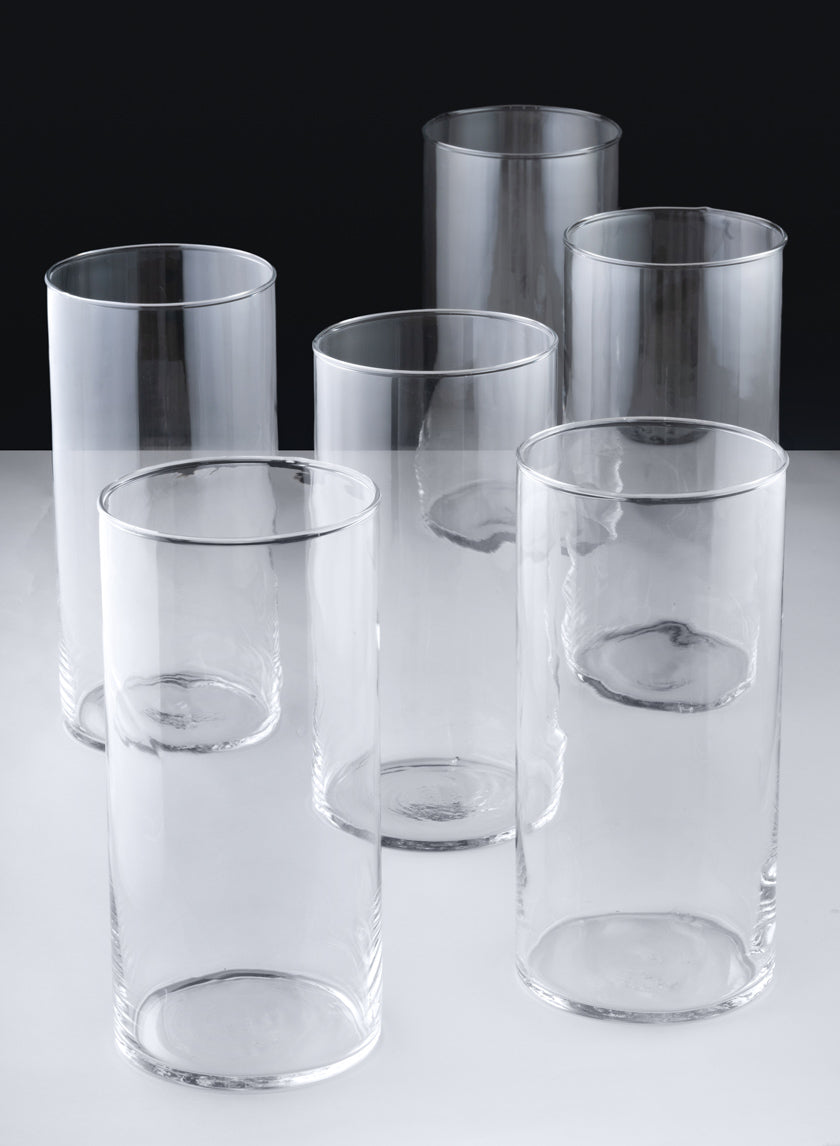 A set of six Best Value Glass Cylinder Vases is arranged in two rows on a light surface with a dark background. The vases are cylindrical, transparent, and display subtle reflections and shadows.