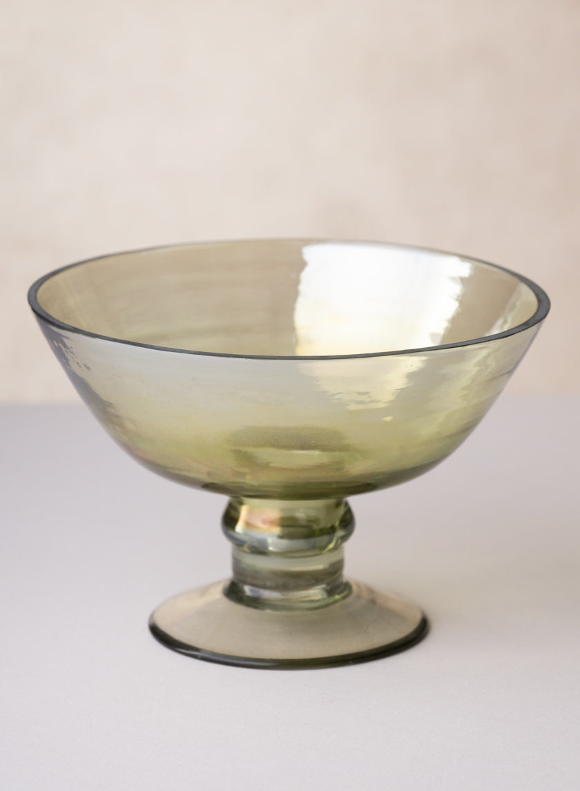 The 6in Wide Malaga Green Luster Glass Flower Compote features a translucent light green finish, a wide rim, and a short pedestal base, shown on a plain surface with a soft, neutral background.
