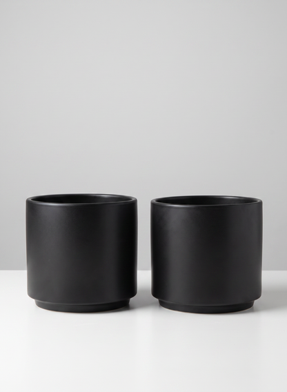Two identical 5.25in Tall Florist Choice Matte Black Cylinder pots, sold as a set of 2, are placed side by side on a white surface against a light gray background.