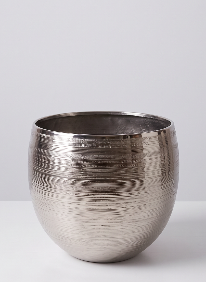 A 15.5in Tall Silver Cache Pot Metal Planter with a round, metallic form and a textured, horizontal lined pattern sits on a white surface against a light gray background.