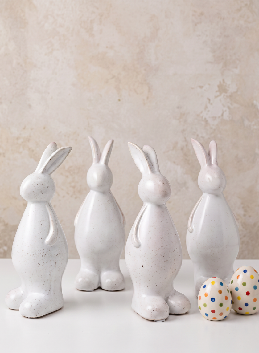 Four 7.5in aged white porcelain rabbits, sold as a set of four, are lined up on a white surface, accompanied by two white eggs decorated with colorful dots. The background is neutral and textured.
