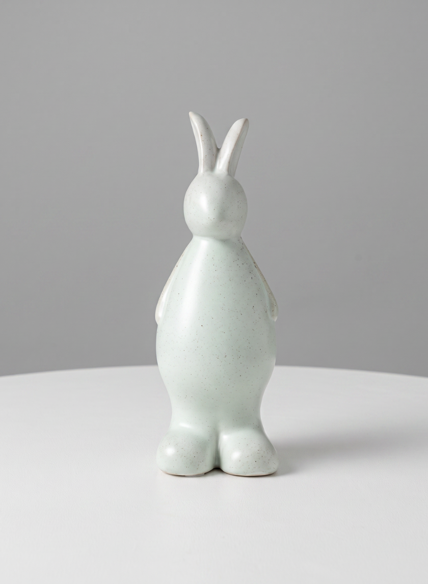 A smooth, minimalistic 7.5-inch aged white porcelain rabbit from a set of four stands upright on a white surface against a plain gray background. The figurine features no facial details and showcases a rounded, modern design.