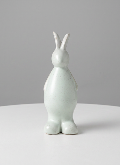 A smooth, minimalistic 7.5-inch aged white porcelain rabbit from a set of four stands upright on a white surface against a plain gray background. The figurine features no facial details and showcases a rounded, modern design.