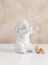 A 6.5in Aged White Porcelain Rabbit from a set of four is displayed sitting upright beside two pastel, polka-dotted eggs on a white surface, with a light beige textured background.