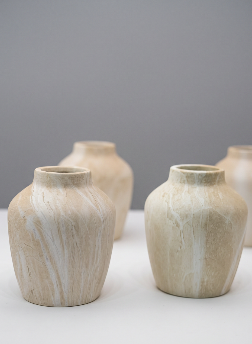 Four 4in tall "Travertine Look" ceramic mini vases, featuring subtle marbled patterns in beige, are arranged on a white surface against a plain gray background. Each vase has a rounded shape and a narrow opening.