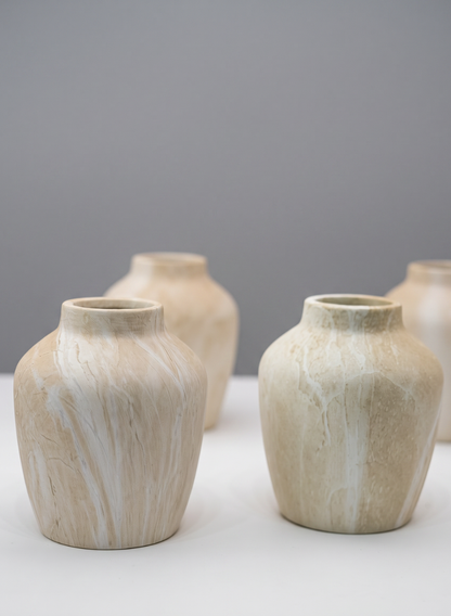Four 4in tall "Travertine Look" ceramic mini vases, featuring subtle marbled patterns in beige, are arranged on a white surface against a plain gray background. Each vase has a rounded shape and a narrow opening.