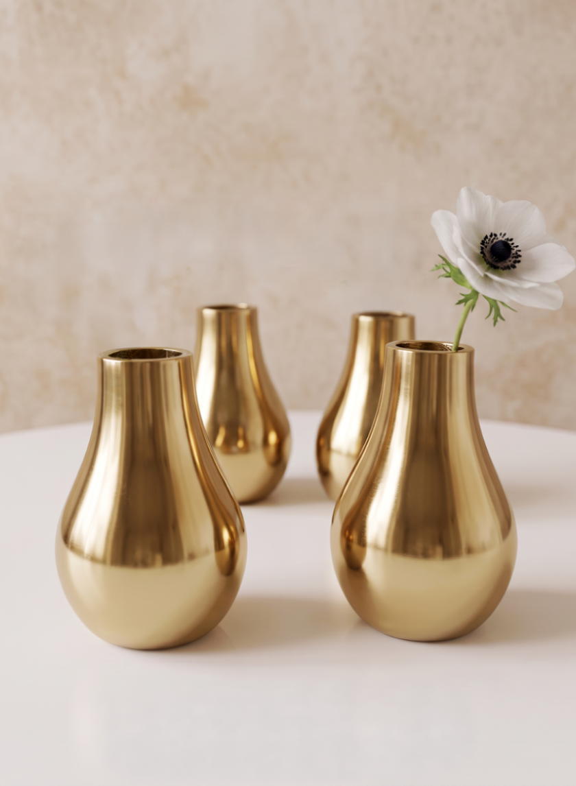 Four 4in Tall Shiny Gold Bud Metal Vases are arranged on a white surface; three stand empty, while one displays a single white flower with a dark center. The scene is set against a softly textured beige background.
