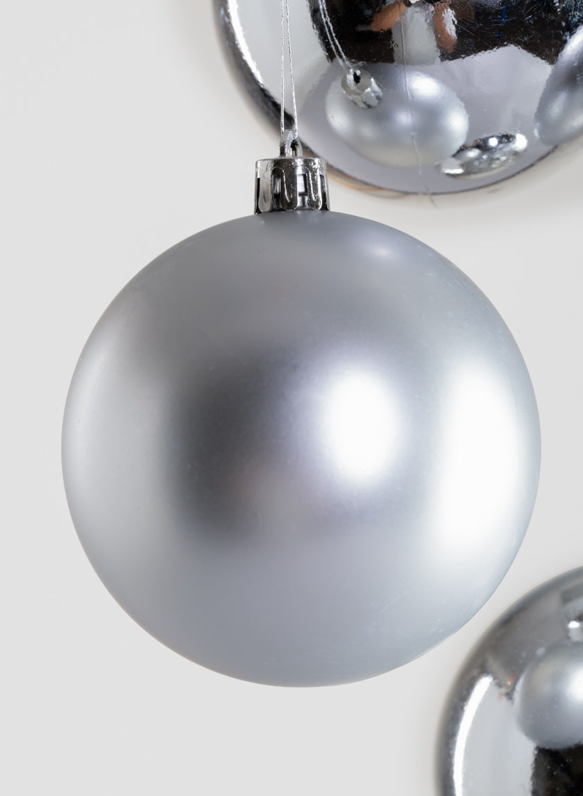 A close-up of the 3in Round Matte &amp; Shiny Silver Ornament Ball hanging with two other silver ornaments partially visible in the background on a light surface.