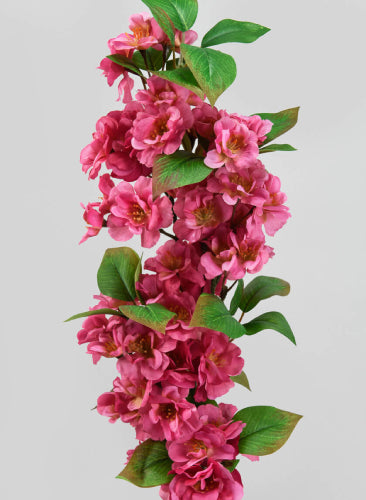 Artificial pink floral branch with green leaves on a light gray background