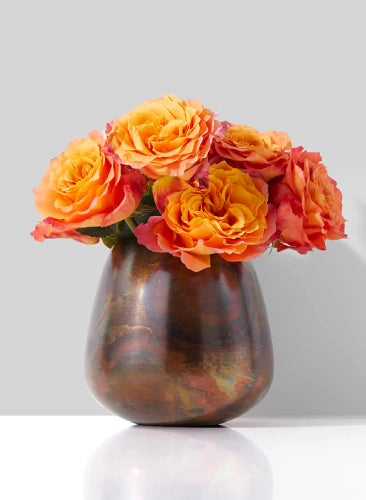 Vase with orange and red flowers on a white surface and light gray background